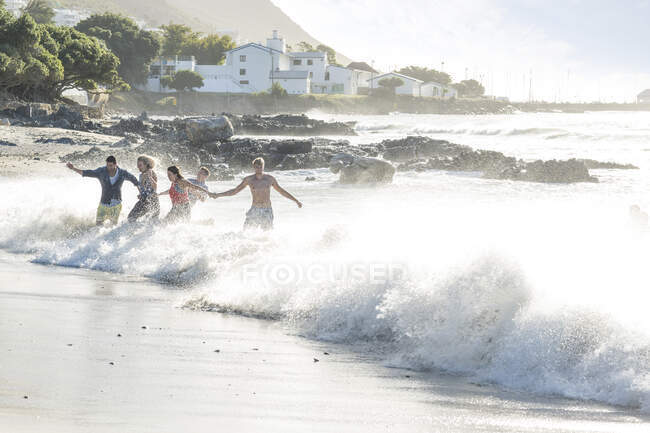 Young adult friends running and splashing through waves at beach party — Stock Photo