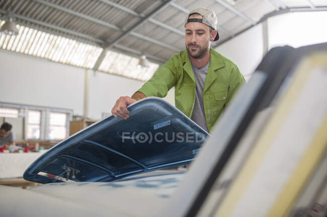 Hombre montaje de la pieza de coche en taller de reparación de carrocería - foto de stock
