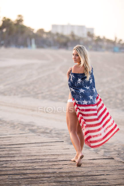 Portrait of sultry young woman wrapped in american flag on boardwalk, Santa Monica, California, USA — Stock Photo