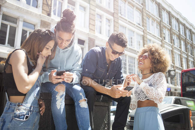 Четыре молодых друга на улице, смотрят на смартфон — стоковое фото
