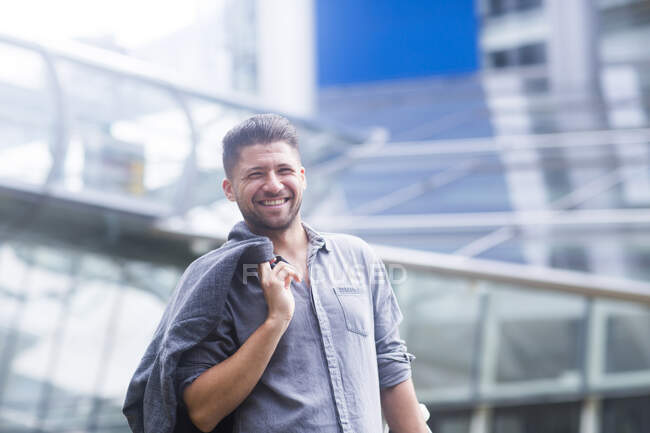Retrato de homem carregando jaqueta sobre ombro e sorrindo para a câmera — Fotografia de Stock