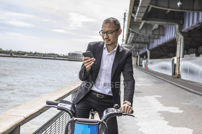 Geschäftsmann Radfahrer schaut auf Smartphone am Wasser — Stockfoto
