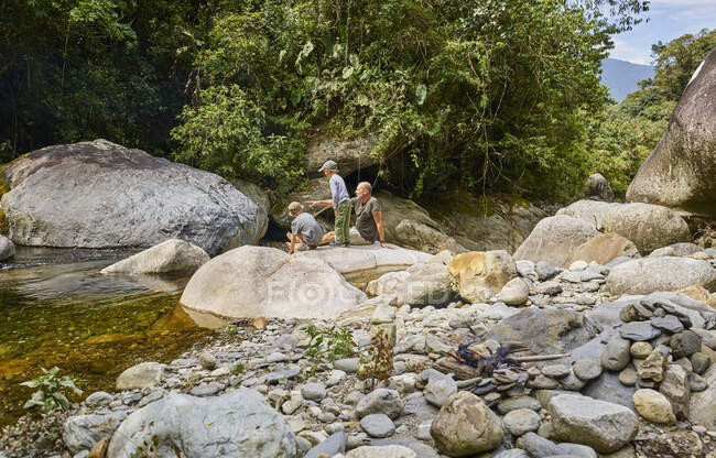 Padre e hijos descansando sobre rocas junto al agua, Ventilla, La Paz, Bolivia, Sudamérica - foto de stock