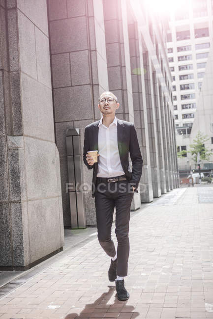 Бизнесмен с кофе на вынос прогуливается по тротуару — стоковое фото