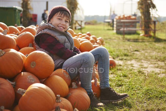 Retrato del niño sentado en una pila de calabazas cosechadas - foto de stock