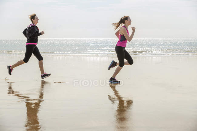 Вид сбоку матери и дочери, бегущих по пляжу — стоковое фото