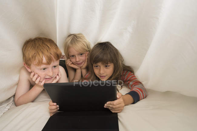 Дети лежат в постели и смотрят на цифровой планшет — стоковое фото