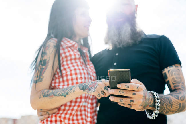 Зрелая татуированная пара хипстеров смотрит на смартфон — стоковое фото