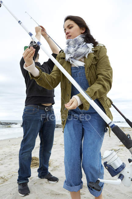Jovem casal preparando varas de pesca do mar na praia — Fotografia de Stock