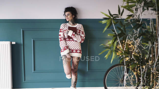 Молодая женщина в рождественском свитере прислонилась к стене — стоковое фото
