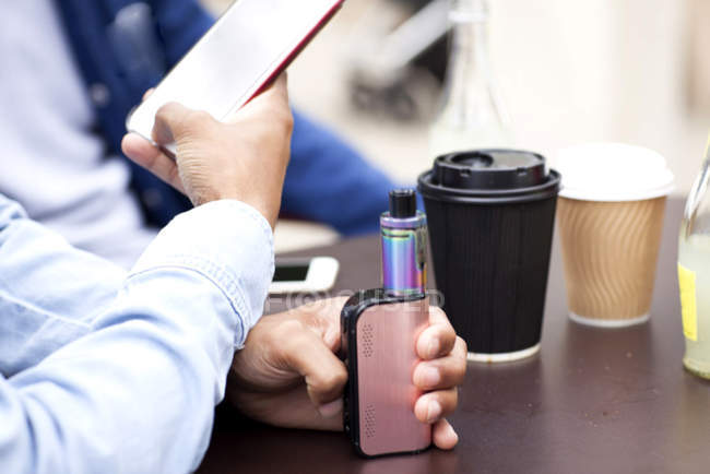 Cropped view of man holding smartphone and vape — Stock Photo