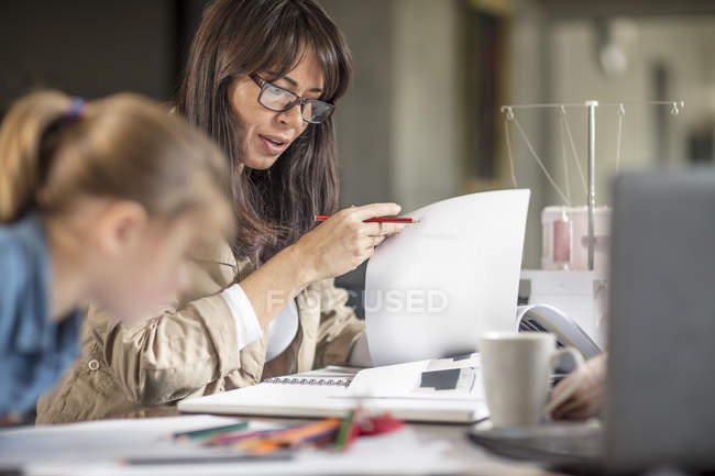 Mulher madura fazendo papelada enquanto filha desenho na mesa — Fotografia de Stock