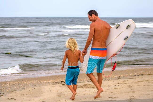 Зрелый серфер и сын, идущий к морю, Эсбери Парк, Нью-Джерси, США — стоковое фото