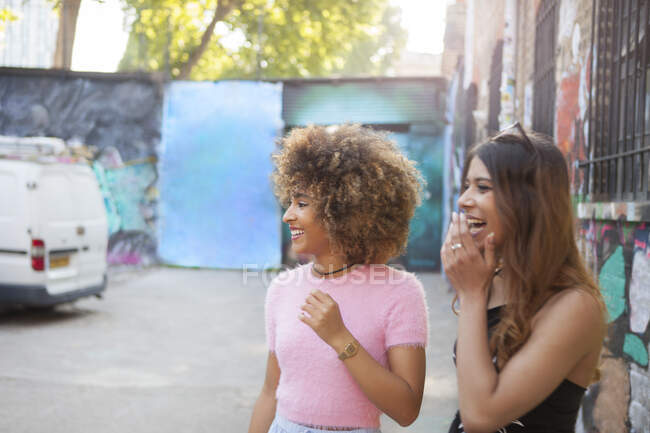 Дві молоді жінки на вулиці, дивлячись в сторону, сміються — стокове фото