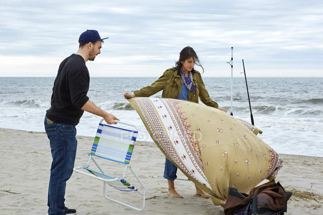 Young fishing couple preparing chair and picnic blanket on beach — Stock Photo