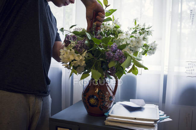 Mid section of young man arranging vase of flowers in front of window — Stock Photo