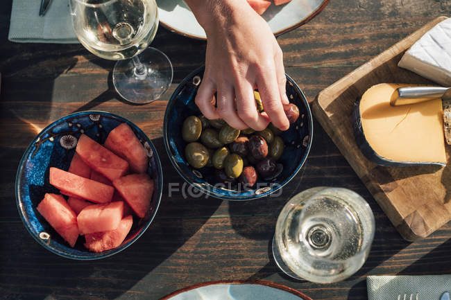 Mão feminina tirando uma azeitona do prato, vista superior — Fotografia de Stock