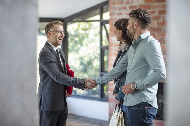 Estate agent shaking hands with couple in empty home — Stock Photo
