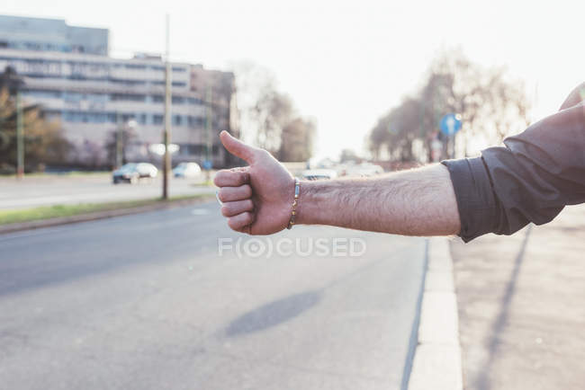 Cropped view of man hitchhiking near road — Stock Photo