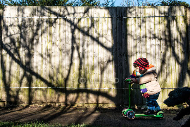 Criança masculina em empurrar scooter no parque iluminado pelo sol — Fotografia de Stock