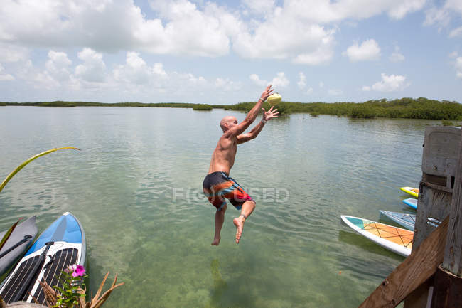 Hombre maduro sumergiéndose en el agua desde la costa - foto de stock