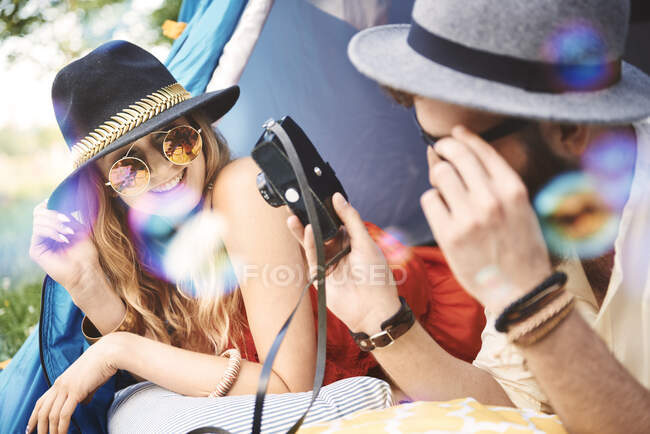 Joven pareja boho tumbada en tienda mirando a la cámara en el festival - foto de stock
