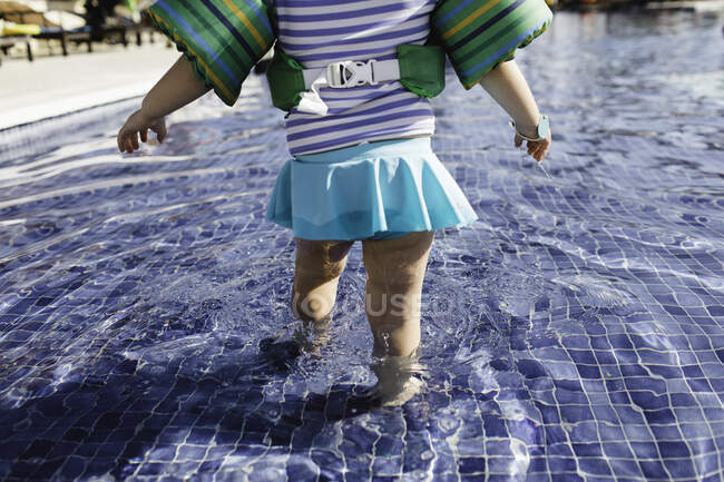 Young girl walking in shallow water in outdoor swimming pool, rear view, low section — Stock Photo