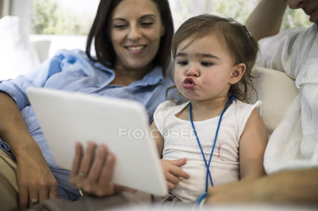 Mari et femme utilisant une tablette numérique avec bébé fille sur canapé — Photo de stock