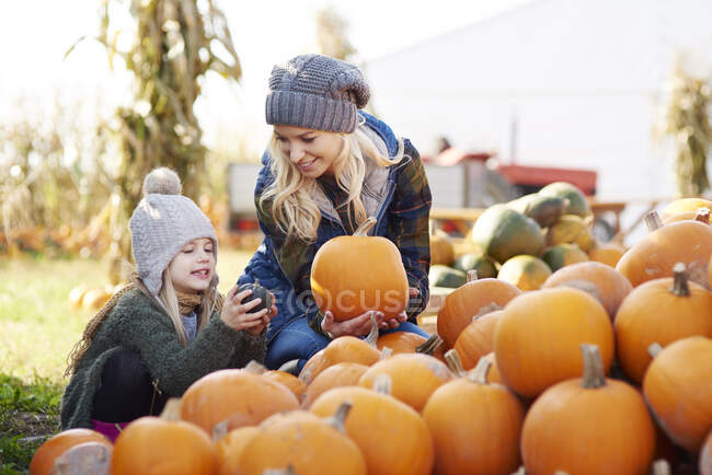 Young woman and daughter selecting pumpkin from stack at pumpkin patch — Stock Photo