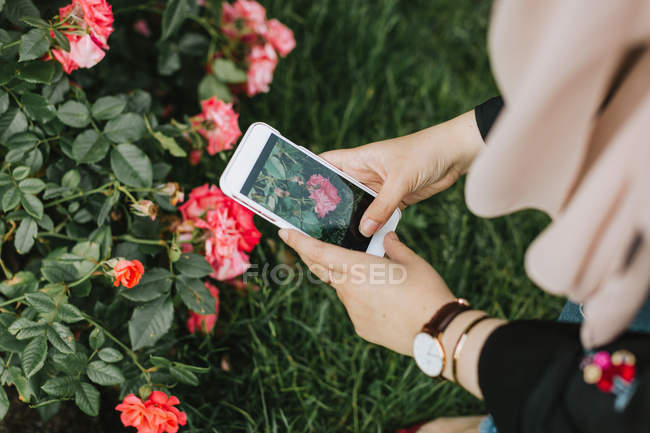 Giovane donna scattare foto fiori su smartphone — Foto stock