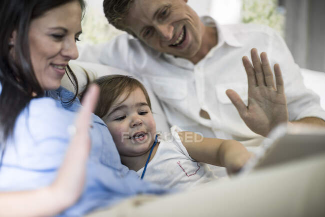 Marido e esposa usando tablet digital com bebê menina no sofá — Fotografia de Stock