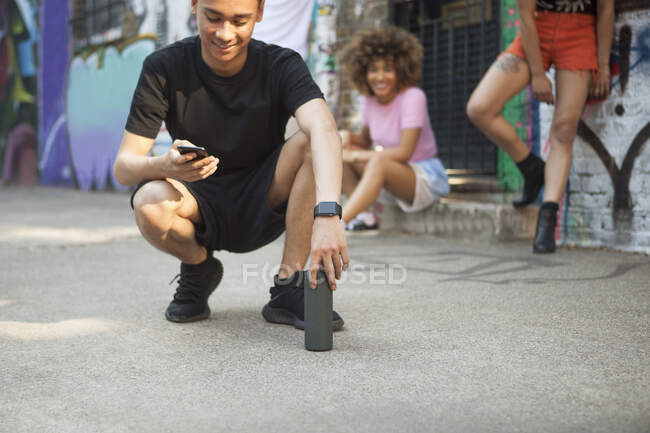 Tre amici appesi in strada, giovane accovacciato, guardando smartphone — Foto stock
