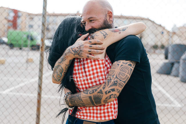 Maduro tatuado hipster casal abraçando por cerca de arame — Fotografia de Stock