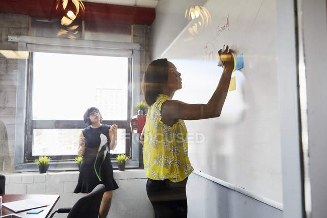 Deux femmes au bureau en utilisant un tableau blanc et des notes collantes — Photo de stock