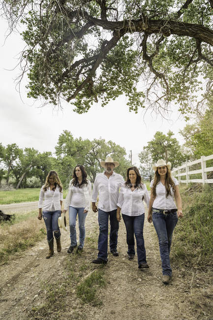 Parejas maduras paseando con mujeres jóvenes a lo largo de la pista de tierra rancho, Bridger, Montana, EE.UU. - foto de stock