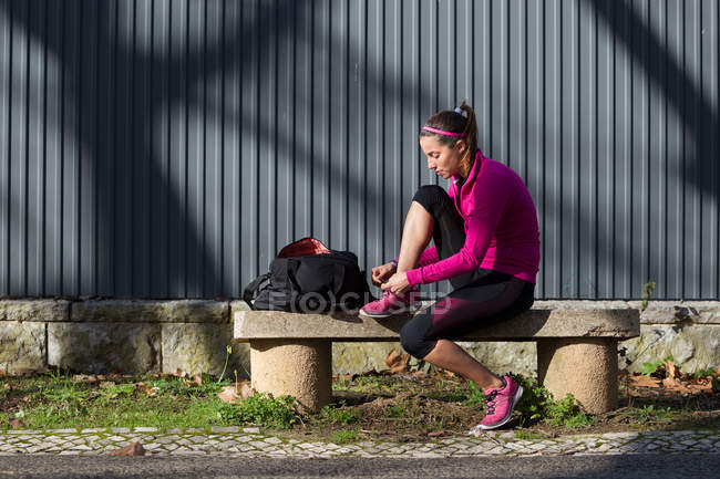 Молодая женщина на скамейке завязывает шнурки на тренировочной обуви — стоковое фото