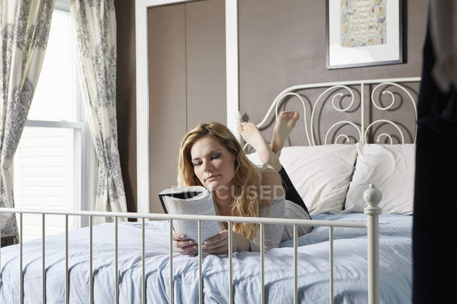 Young woman reading book on bed — Stock Photo