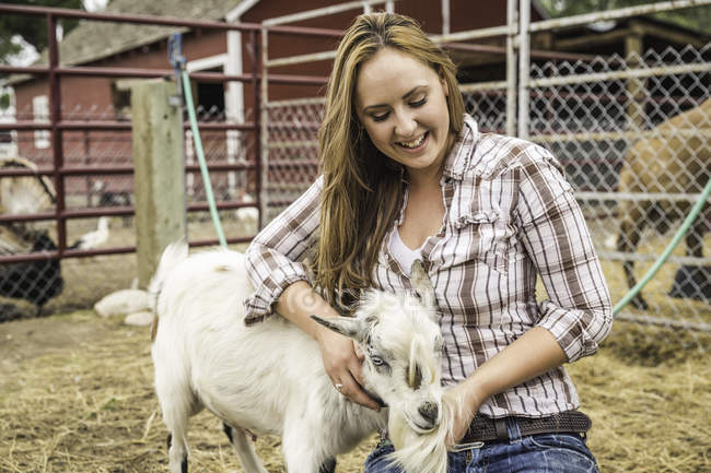 Молодая женщина ласкает козу на ранчо, Бриджер, Монтана, США — стоковое фото