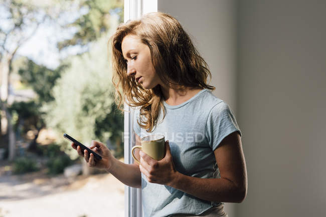 Jeune femme à la porte patio regardant smartphone — Photo de stock
