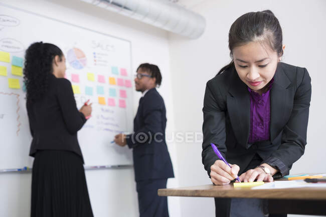 Homme d'affaires et femmes d'affaires, au bureau, remue-méninges, coller des idées au tableau blanc — Photo de stock