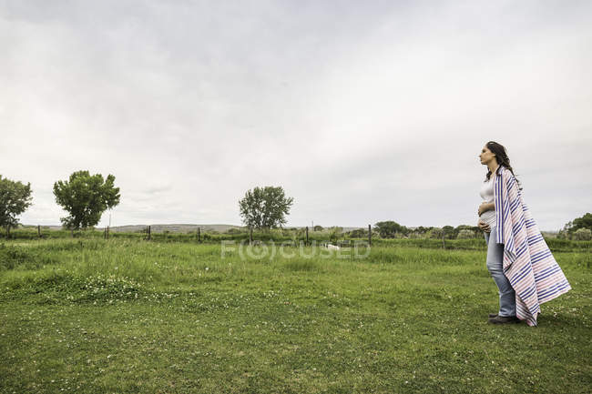 Schwangere junge Frau steht auf dem Feld, Decke um die Schultern, nachdenklicher Ausdruck — Stockfoto