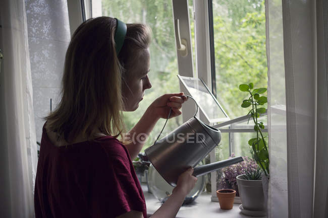 Молода жінка поливає горщики на підвіконні — стокове фото
