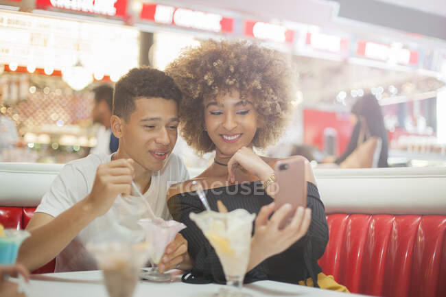 Junges Paar sitzt im Abendessen, schaut aufs Smartphone und lacht — Stockfoto