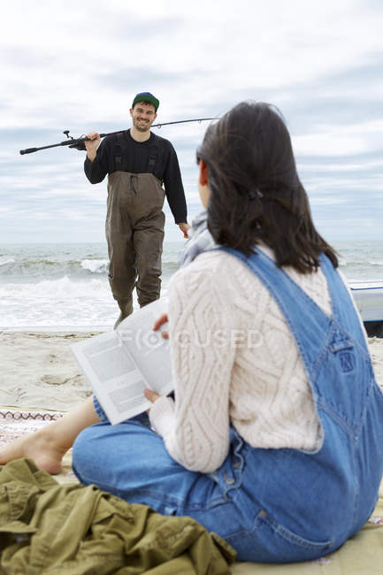 Junge Frau sieht ihren Freund am Strand beim Angeln an — Stockfoto
