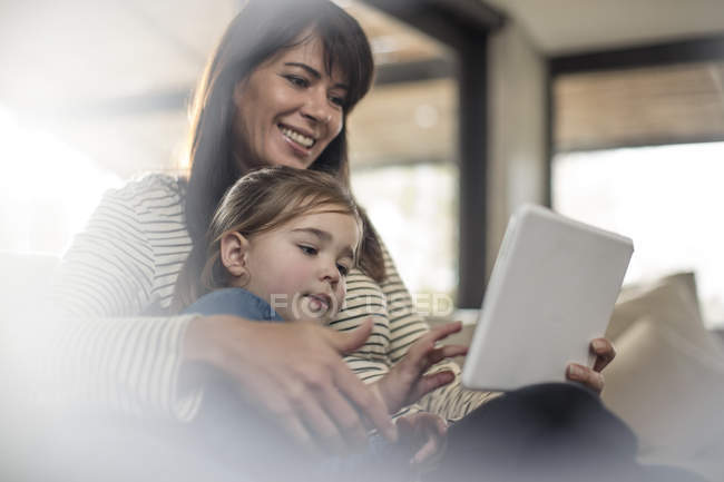 Frau mit Tochter auf Sofa mit Blick auf digitales Tablet — Stockfoto
