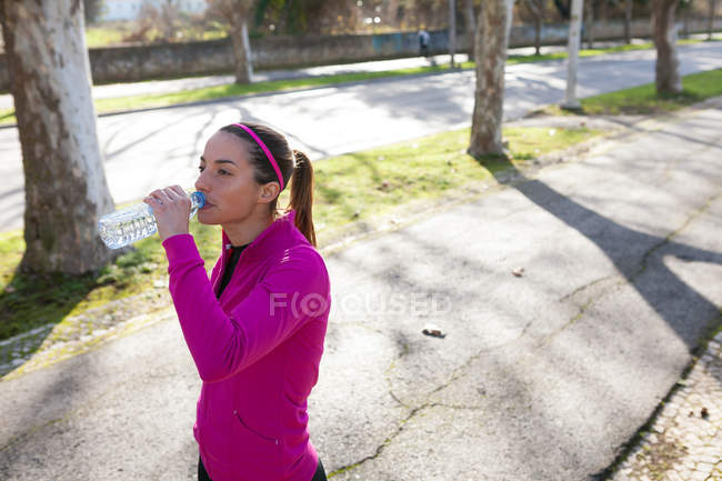 Молодая женщина на улице пьет воду из бутылки — стоковое фото