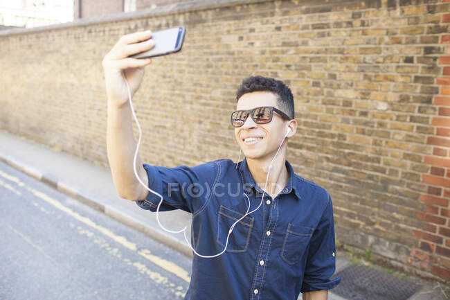 Молодой человек на улице, делает селфи, используя смартфон — стоковое фото