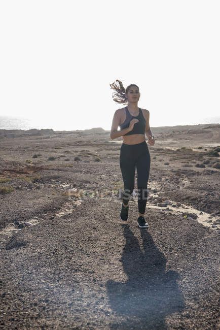 Mujer joven corriendo en un paisaje costero árido - foto de stock