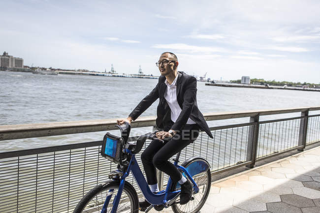 Vista lateral del hombre de negocios en bicicleta en el paseo marítimo - foto de stock