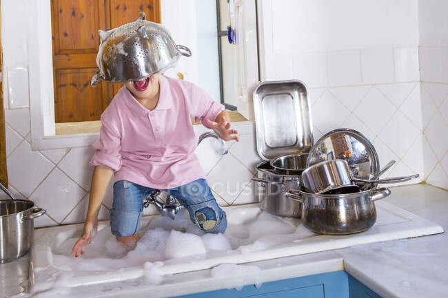 Garçon jouant dans l'évier de cuisine avec passoire sur la tête — Photo de stock